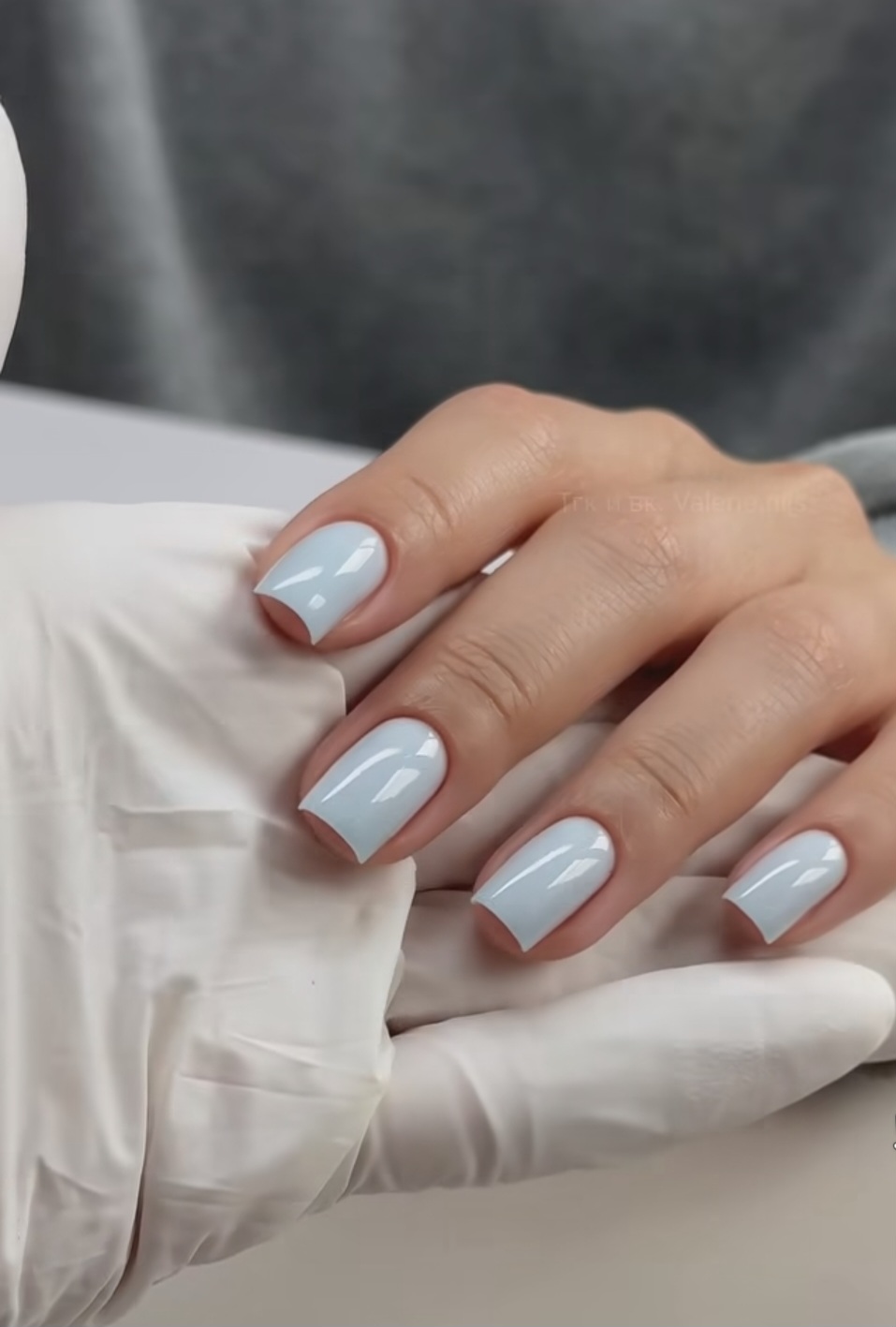 Lichtgrijze gel nagels, net klaar, op een hand in een witte handschoen